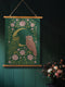 26x36 inch vertical wall tapestry printed on silky polyester, featuring a pair of embroidered-style owls perched on a golden crescent moon, surrounded by pink vintage-style florals and greenery on a forest green background. Includes stained wood slats and twine for easy hanging. A romantic, nature-inspired design for woodland and cottagecore decor lovers.